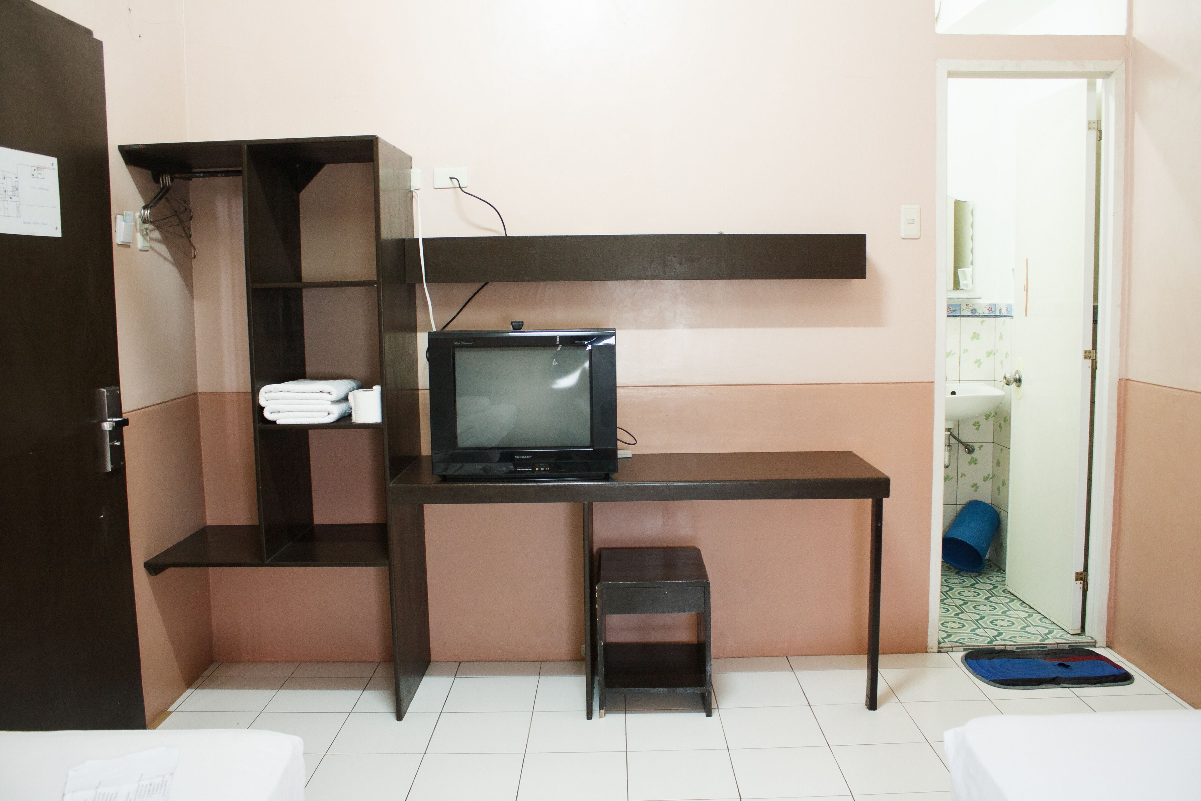 Una habitación pequeña y funcional con cama, escritorio con televisor y un taburete.