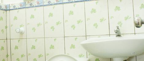 Un baño con inodoro, lavamanos y un cubo rojo.