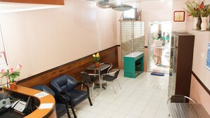 Een receptiegedeelte met een balie, stoelen, een tafeltje met bloemen en een spiegel.