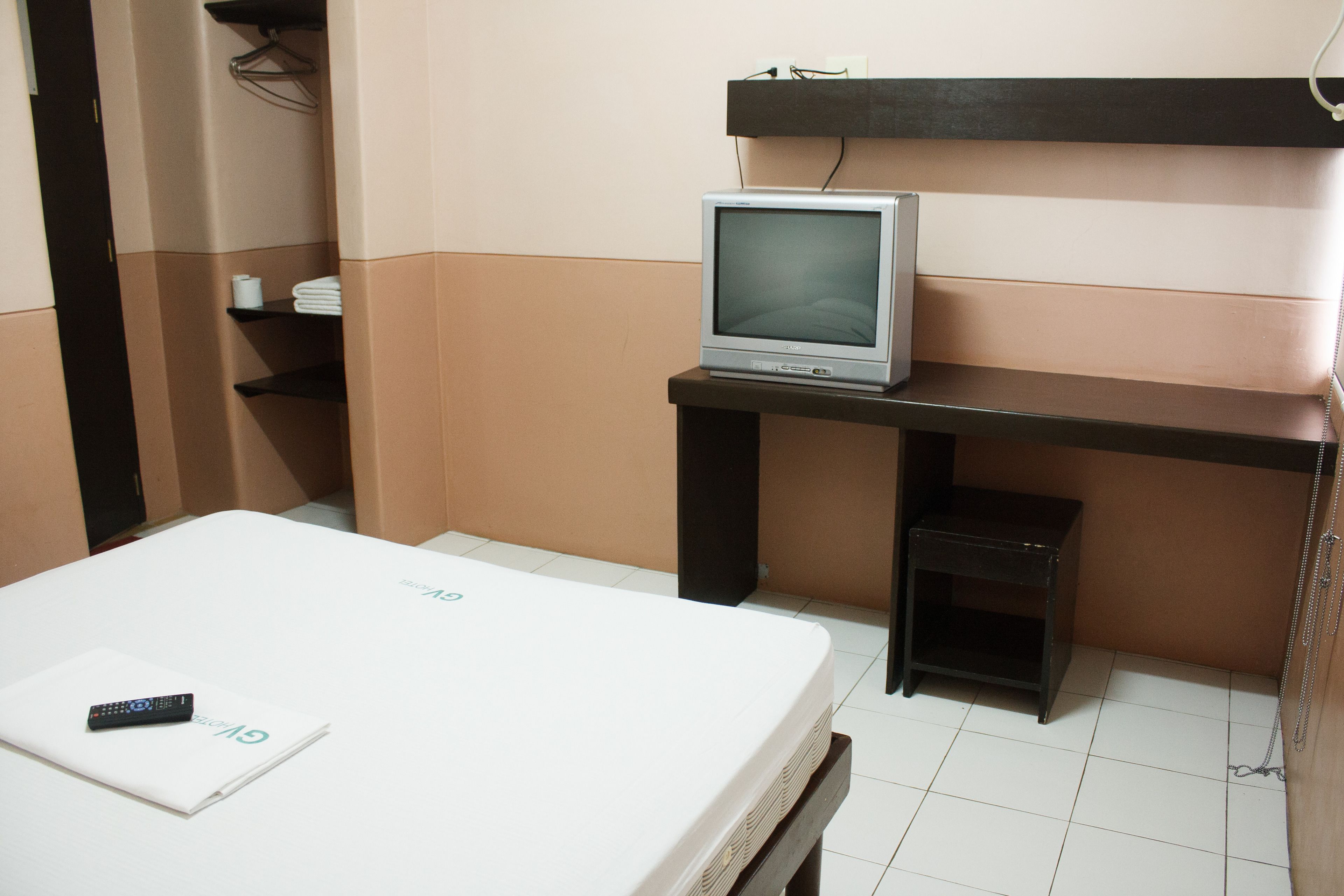 Habitación de hotel con una cama, un pequeño televisor sobre un soporte, un control remoto y una revista sobre la cama.