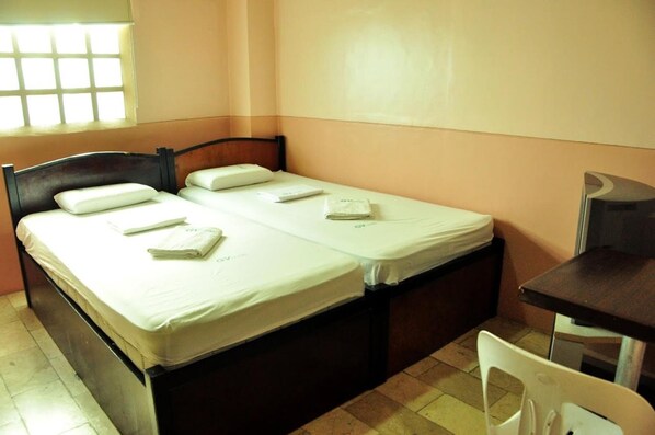 A single bed with white linens and pillows, a small table, and a chair in a room with peach walls and a window with a grid pattern. - GV Hotel Camiguin (Mambajao)
