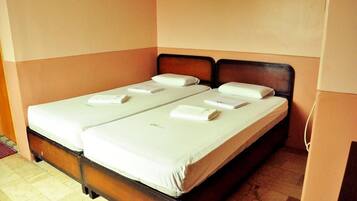 A double bed with white linens and pillows, a wooden headboard, and a tiled floor.
