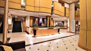 Un vestíbulo de hotel con una recepción, una escalera y una zona de estar.