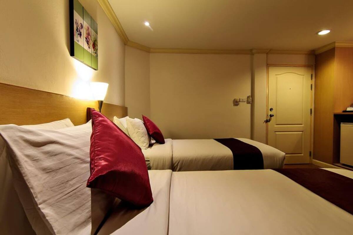 A hotel room with two beds, a nightstand, a lamp, and a door.