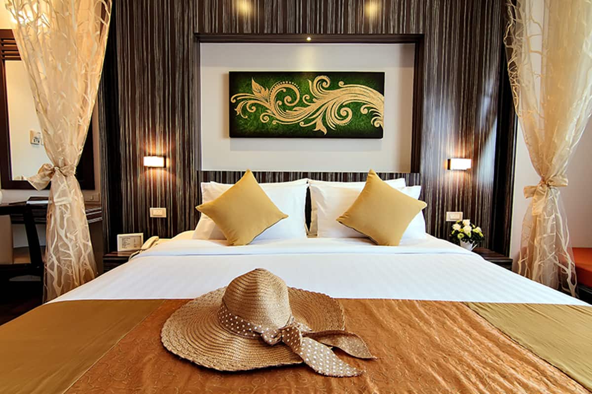 A hotel room with a bed, two pillows, a decorative wall piece, and a hat on the bed.