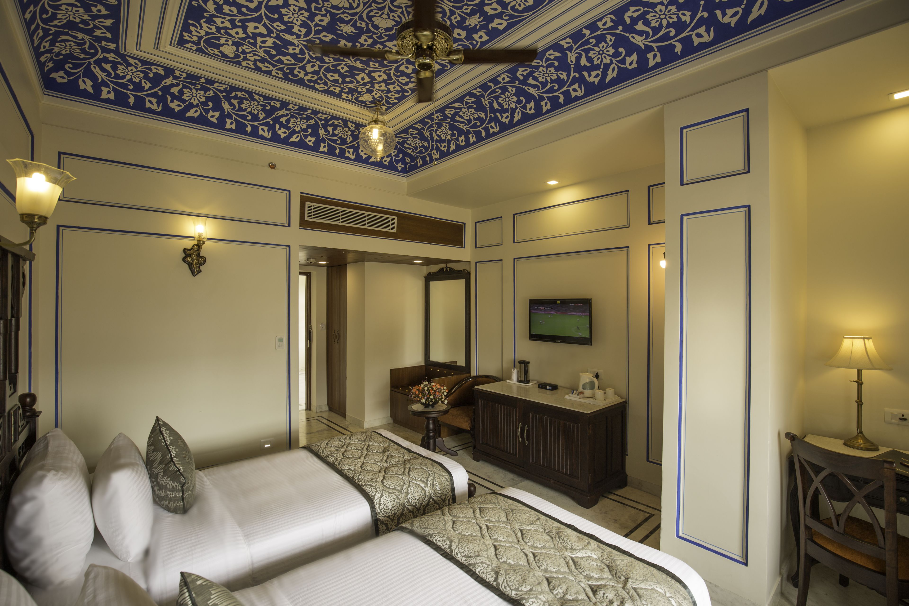 A hotel room with two beds, a dresser, a television, and a ceiling fan.