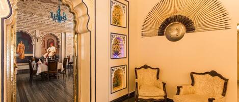 Una habitación con decoración elaborada, que incluye un espejo que refleja un comedor, obras de arte enmarcadas y un abanico decorativo.