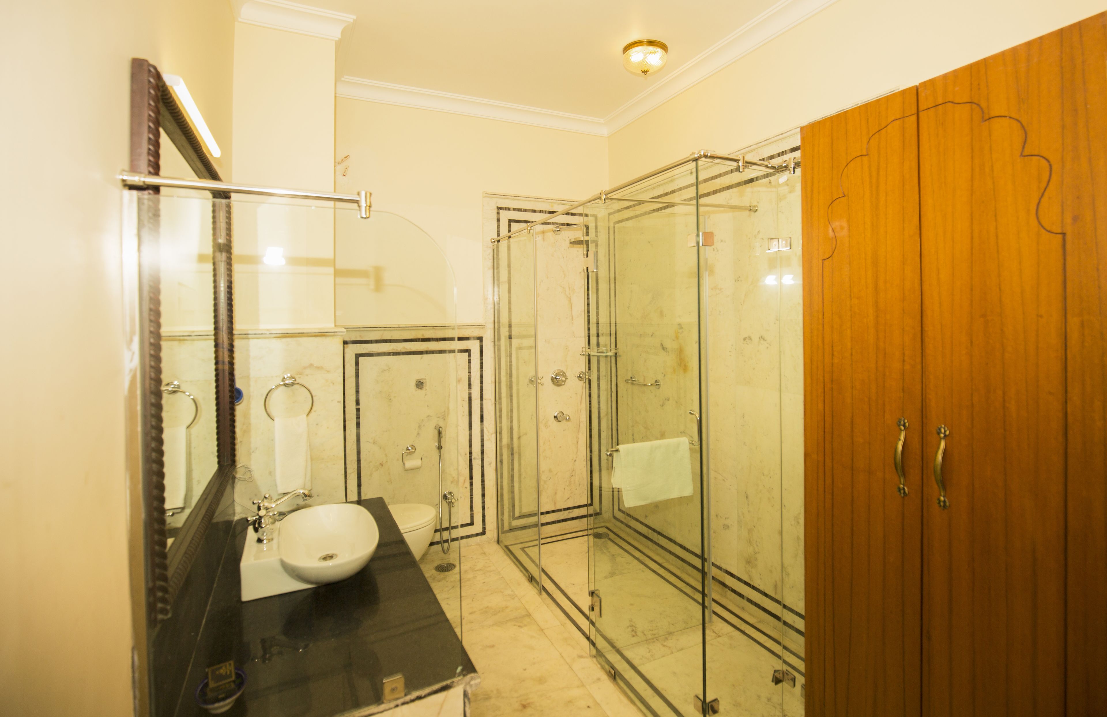A bathroom with a glass-enclosed shower, a sink, and a wooden wardrobe.