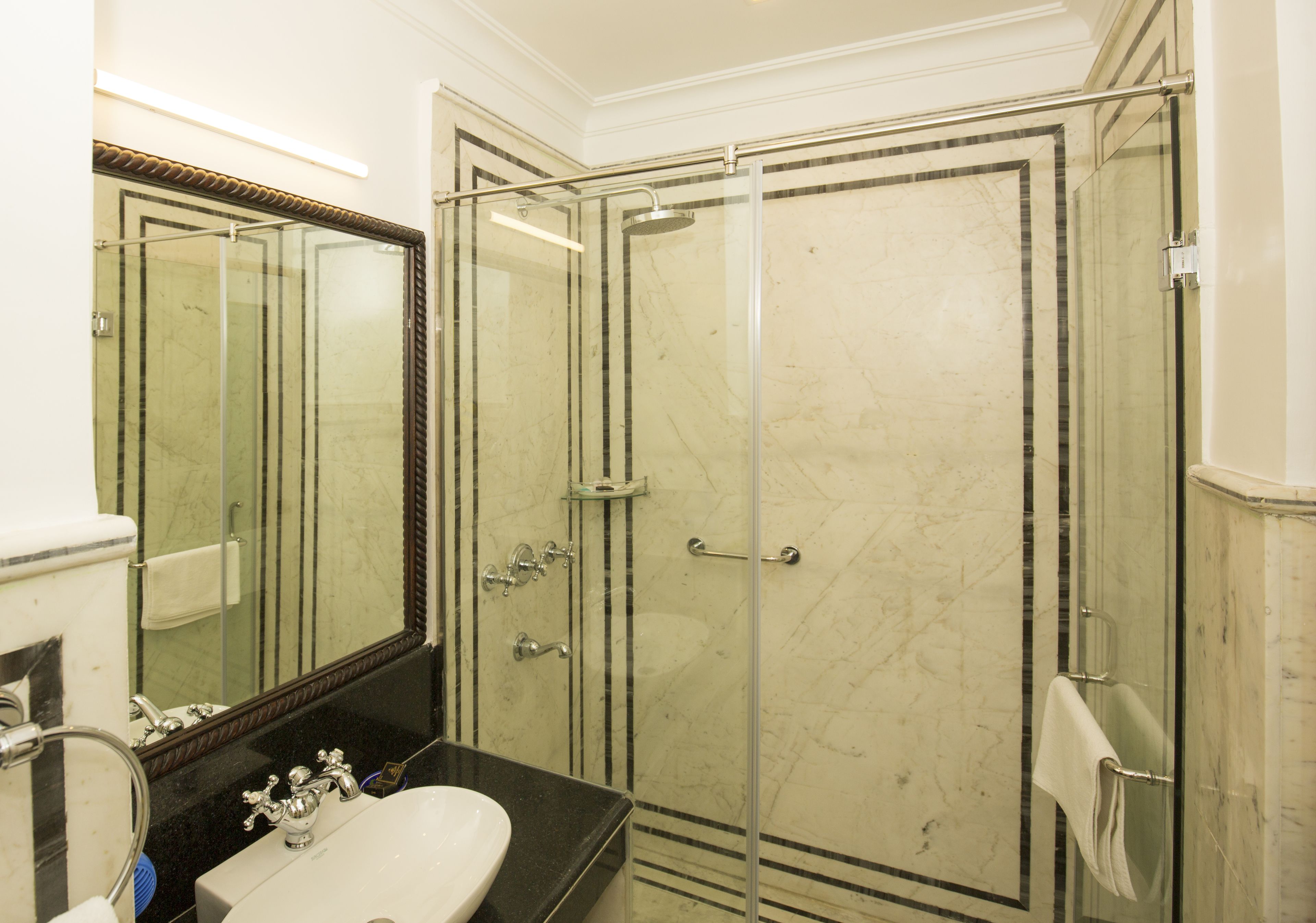 Un baño con ducha envuelta en vidrio, un lavabo con espejo y un perchero para toallas.