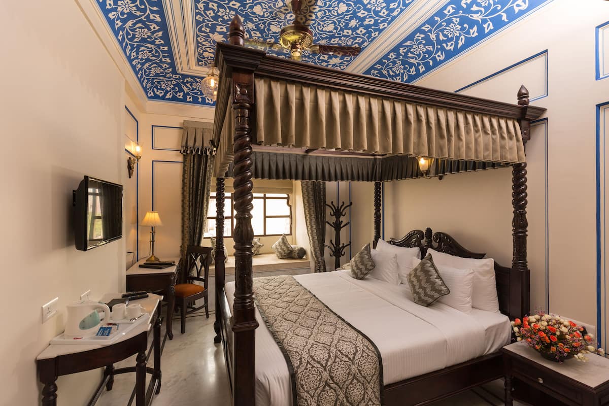 A four-poster bed with a canopy, a bedside table with a lamp, a small table with a tray of toiletries, and a flower arrangement on the nightstand.