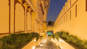 A corridor with a wooden staircase leading to a building entrance, flanked by walls with traditional architectural details.