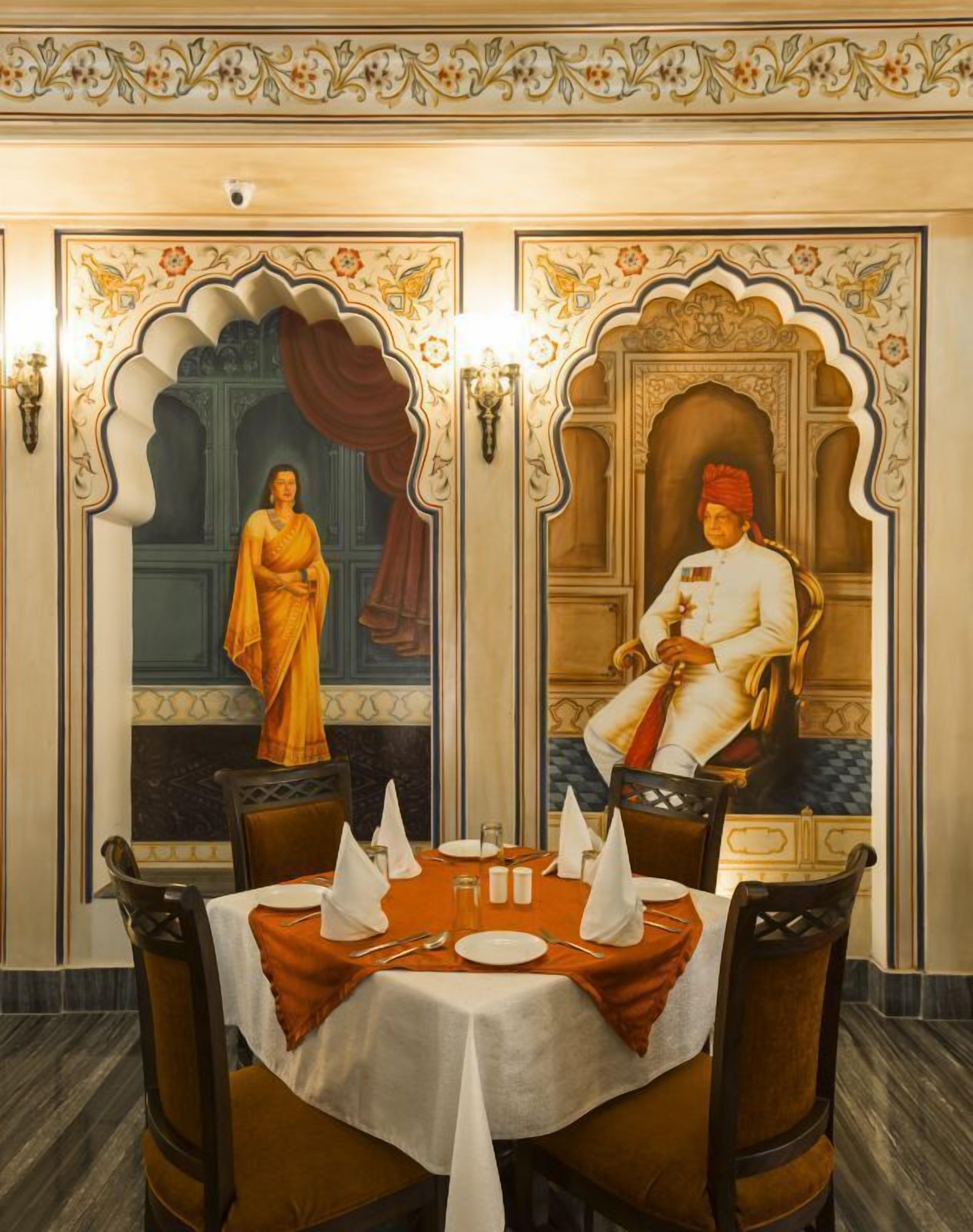 A dining area with a table set for two, ornate wall decorations, and a large mirror reflecting the room.