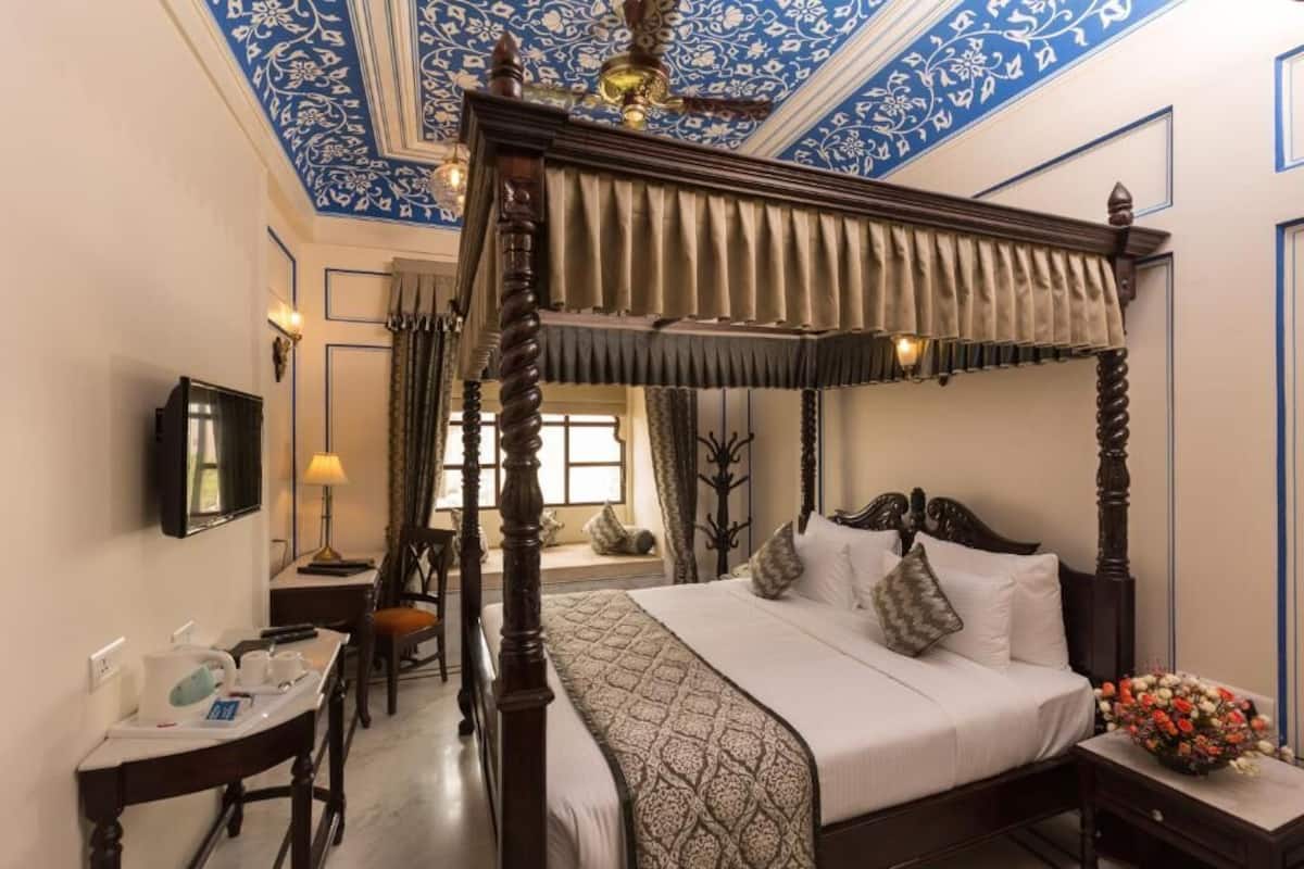 Una cama con dosel, una mesita de noche con lámpara, un escritorio con silla y un televisor en la pared.
