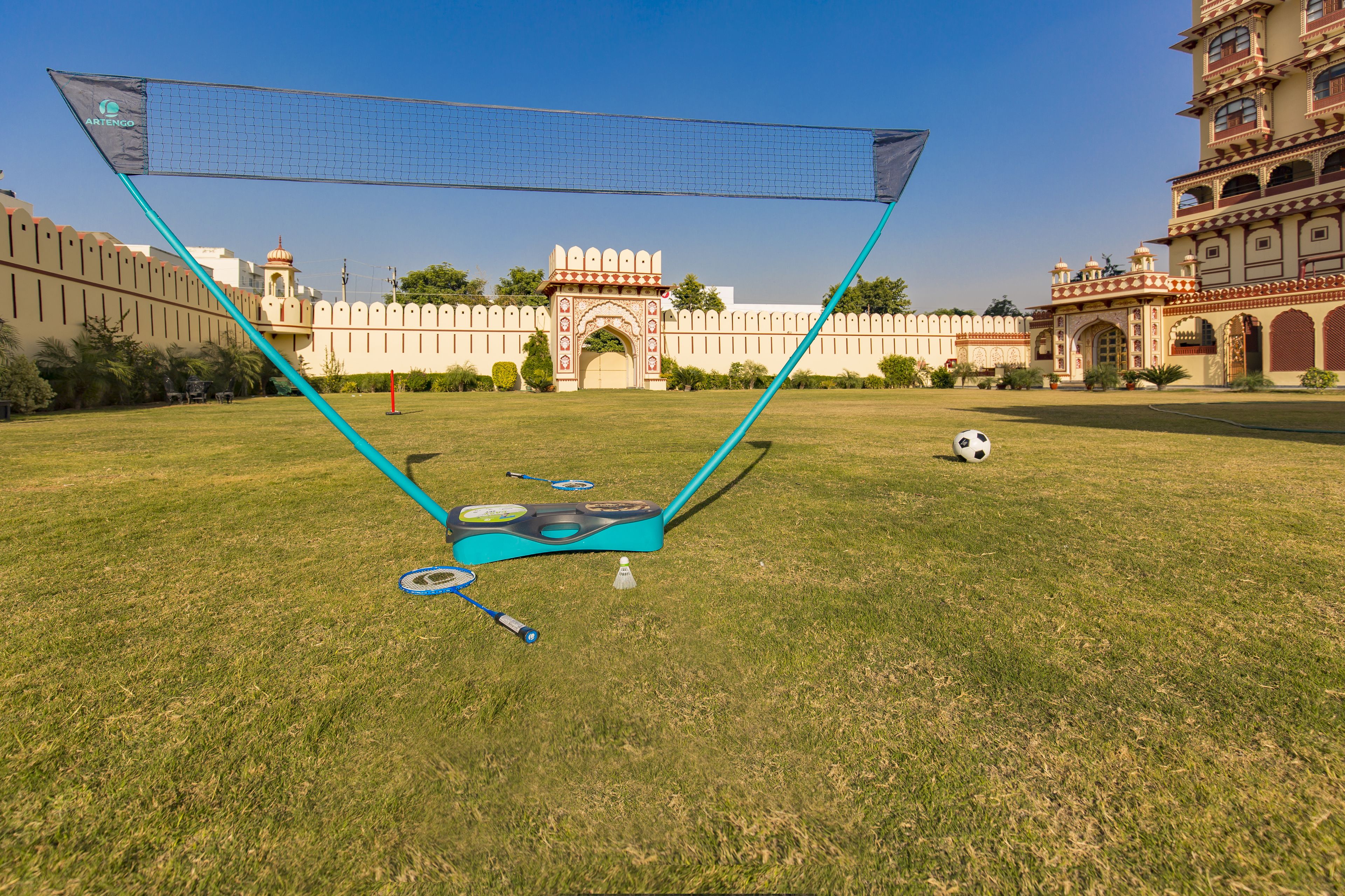 A netted area with a soccer ball and goalposts in a grassy field with a historic building in the background.