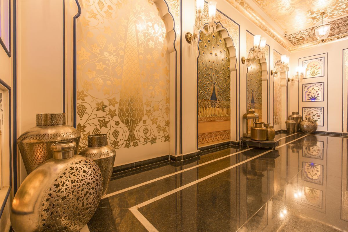 Un pasillo lujoso con diseños ornamentales en las paredes, grandes jarrones decorativos e iluminación elegante.