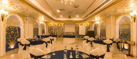 Un salón de conferencias con mesas redondas, sillas blancas y una araña de cristal.