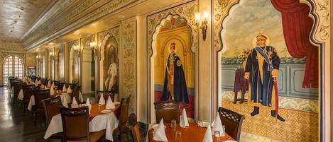 Un restaurante con murales ornamentales y candelabros, que presenta un amplio comedor con mesas dispuestas para los comensales.