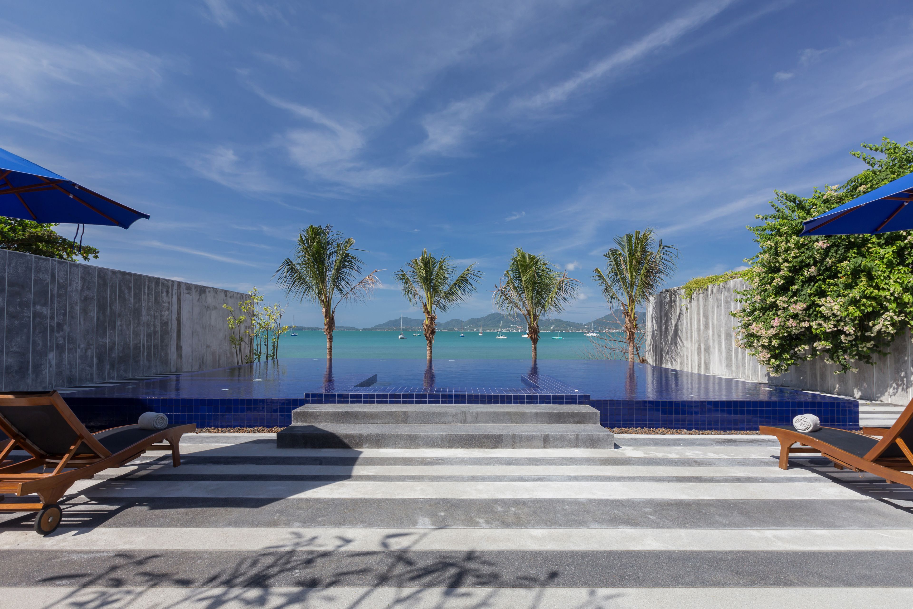 A poolside area with lounge chairs and umbrellas, a clear view of the ocean, and a tiled infinity pool.
