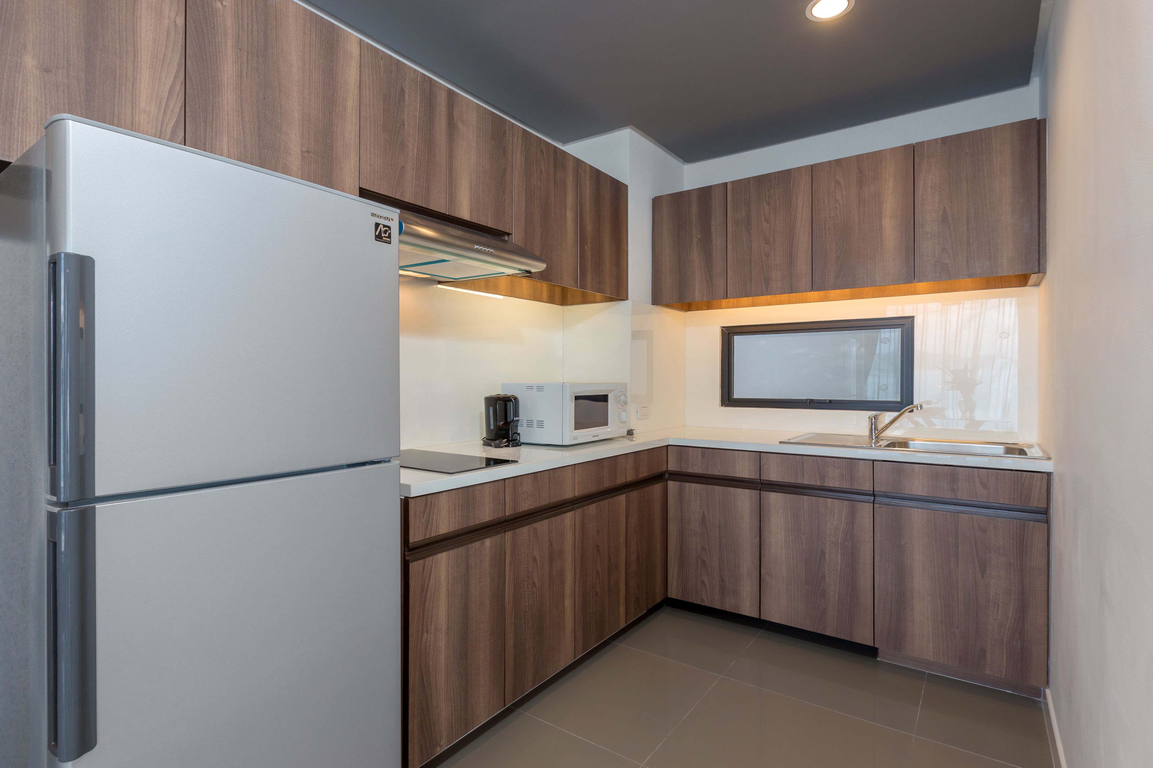 A modern kitchen with wooden cabinets, a stainless steel refrigerator, a microwave, and a coffee maker.