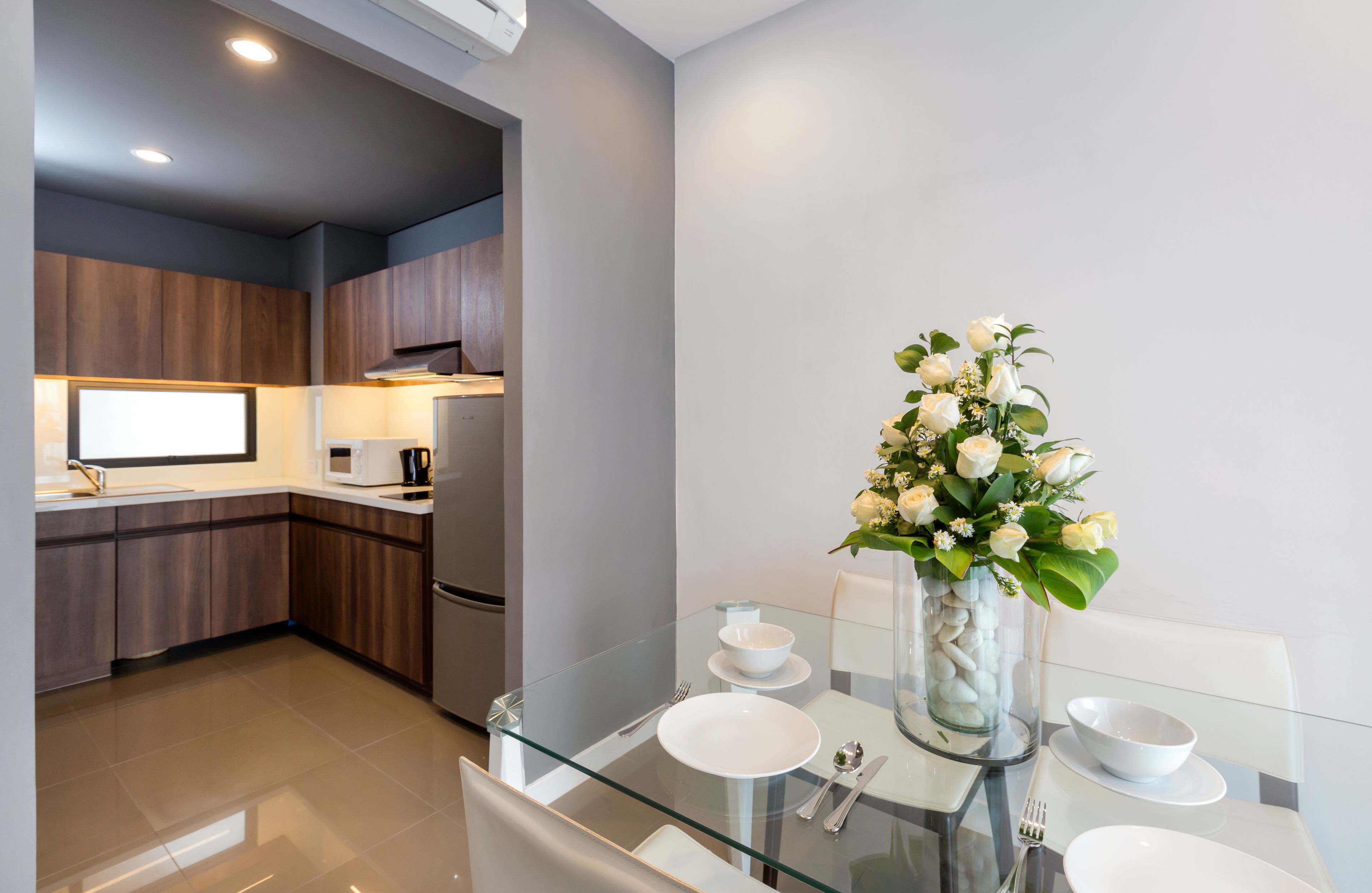A modern kitchen with dark wood cabinets, a glass dining table with white plates, and a vase of white flowers.