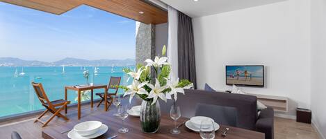 A dining area with a view of the sea, a large vase with flowers, and a television on the wall.