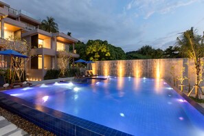 A modern pool area with a clear blue pool, lounge chairs, and a waterfall feature.