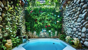 A hot tub surrounded by a stone wall with greenery and decorative frogs.