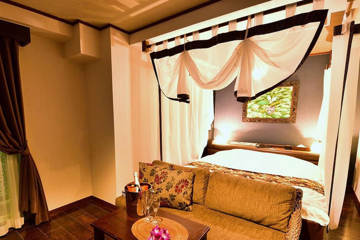 Un dormitorio con cama, sofá, mesita de noche y ventana con vistas a zonas verdes.