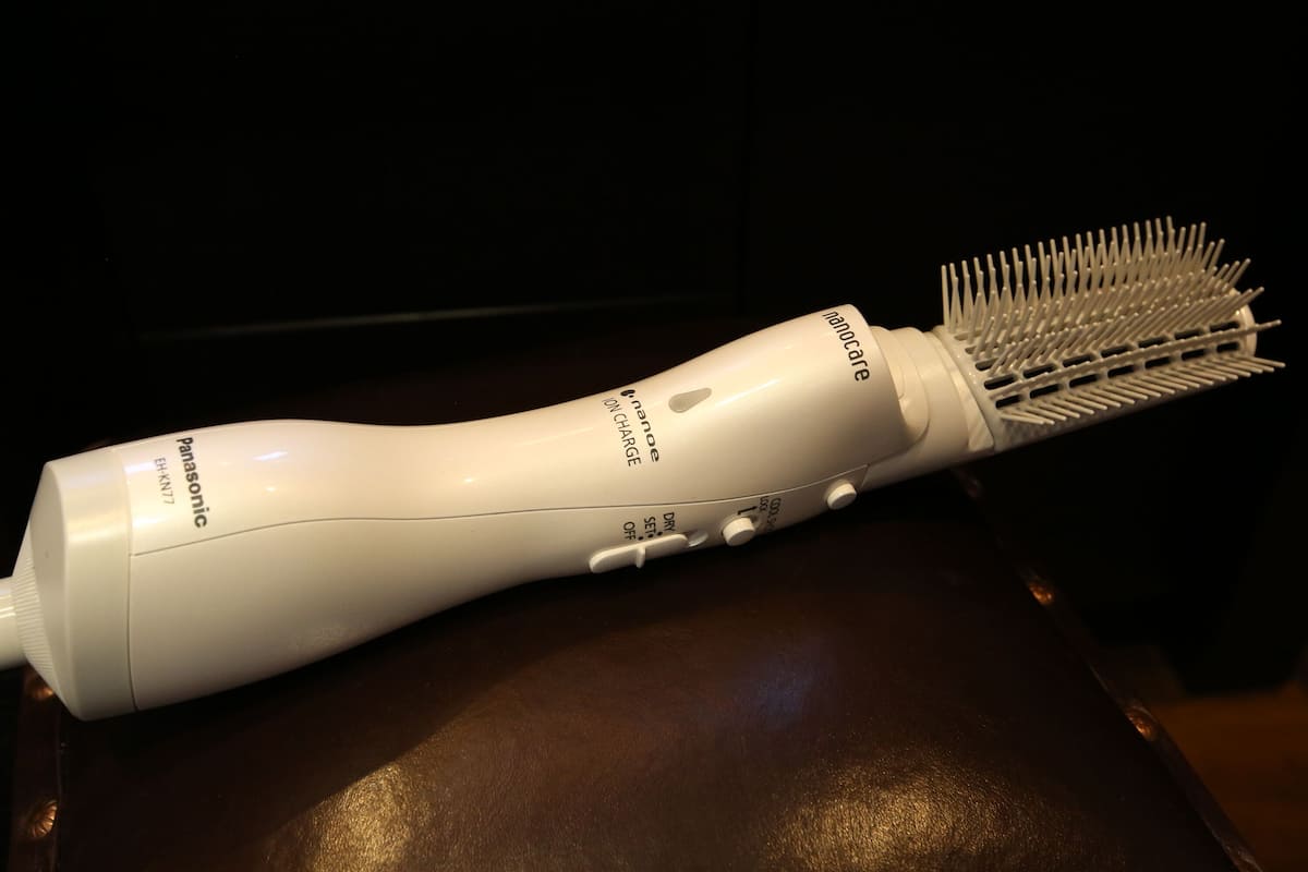 Secador de pelo blanco con base de carga y accesorio cepillo sobre una superficie oscura.