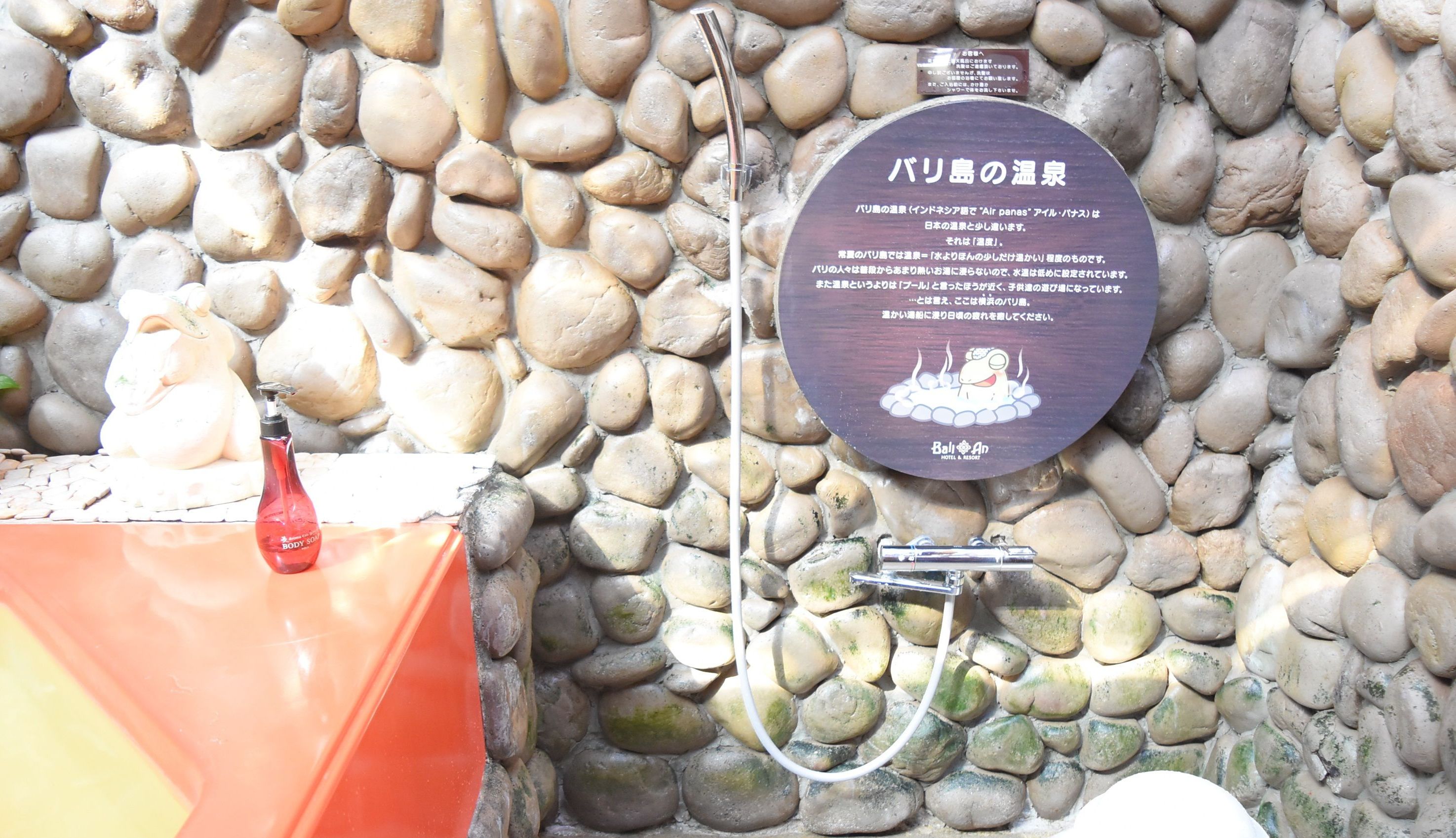 A stone wall with a hot spring sign and a statue of a cat.