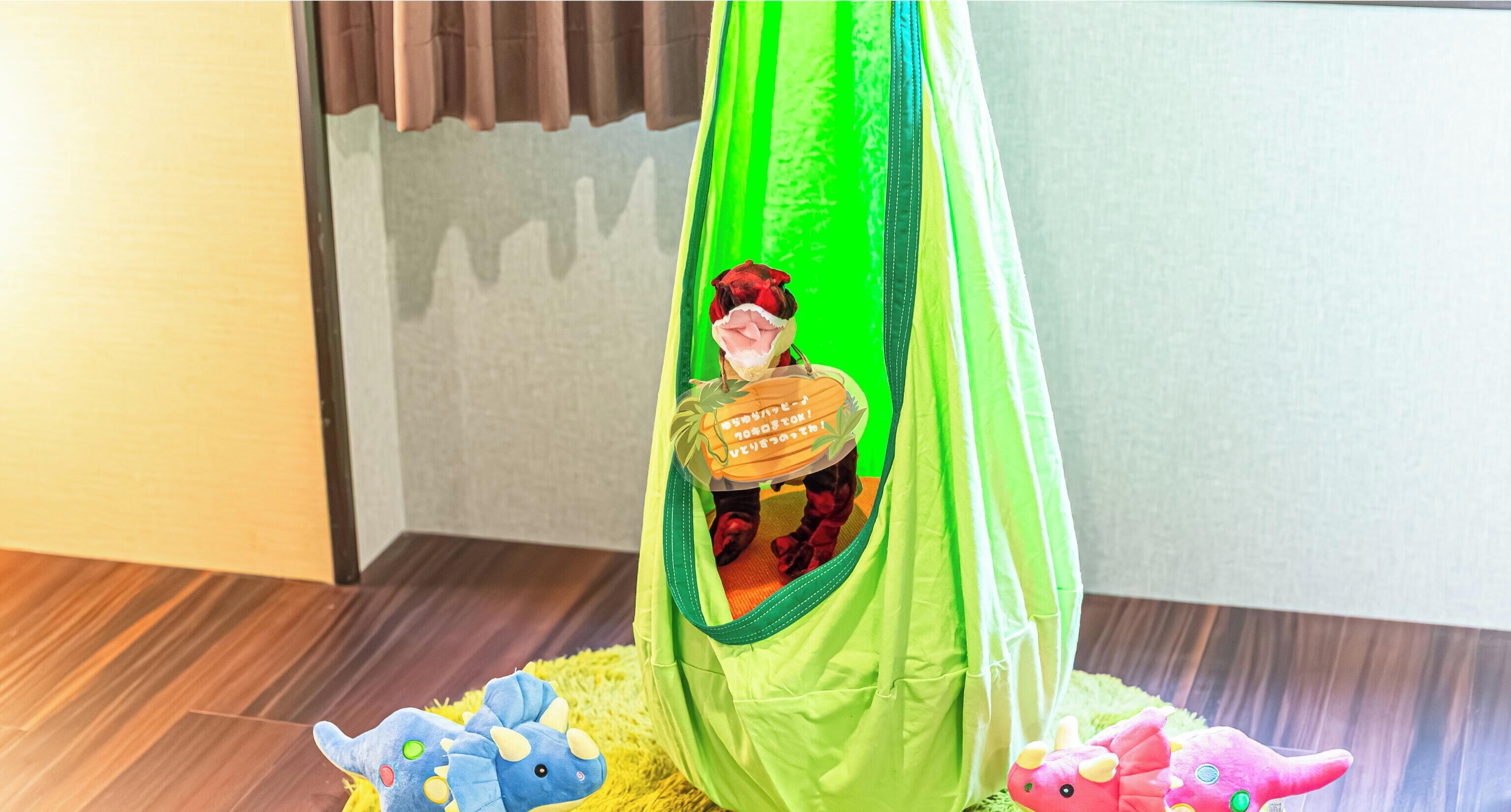 A green tent-like structure with a toy inside, placed on a wooden floor with a yellow rug.