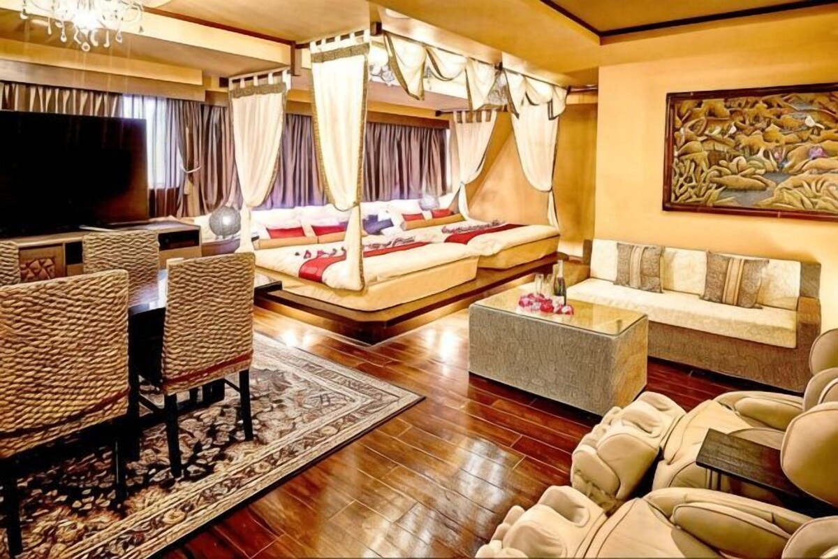 A hotel room with a four-poster bed, a sofa, a coffee table, and a television.