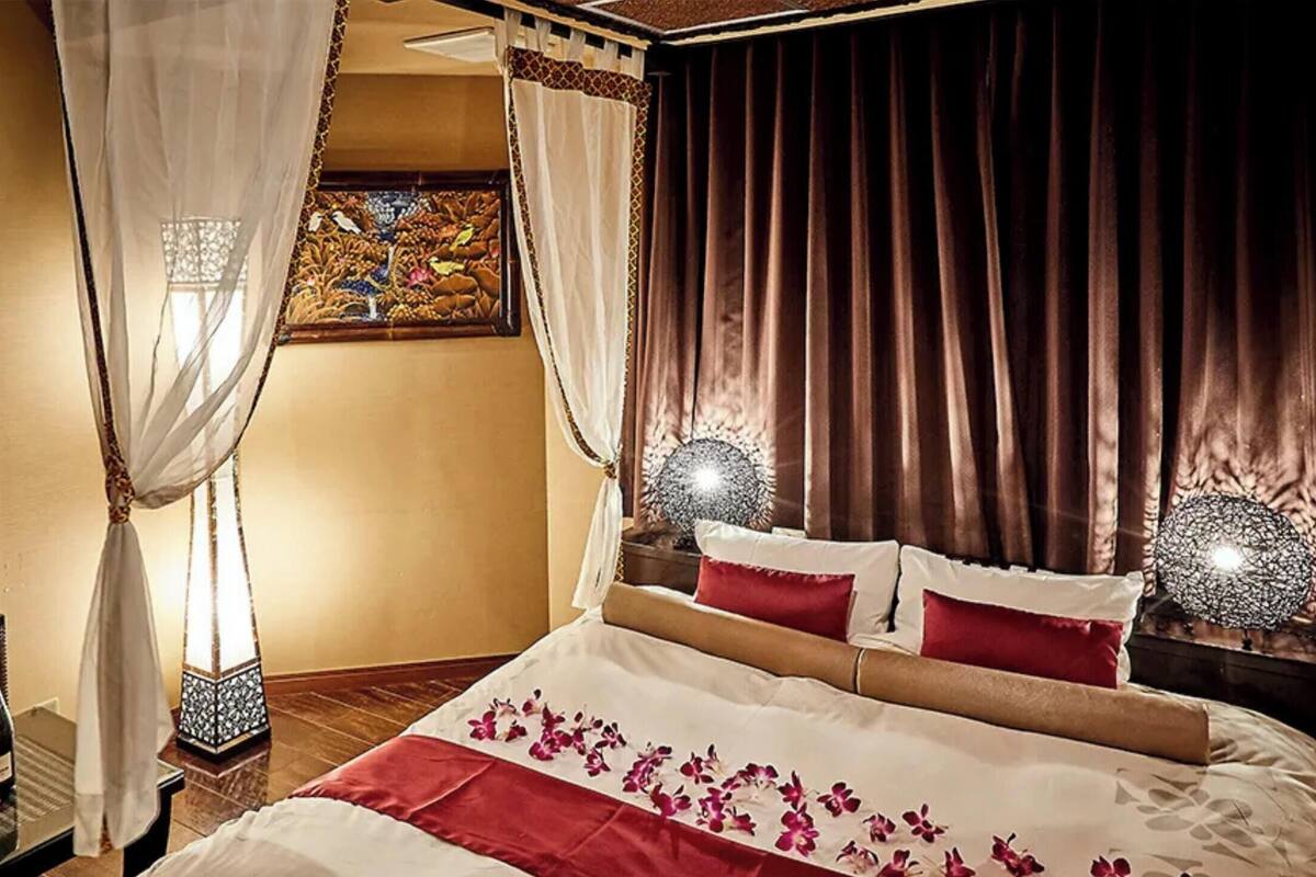 Ein Hotelzimmer mit Bett, Nachttisch, Lampe und einem Fenster mit Vorhängen.