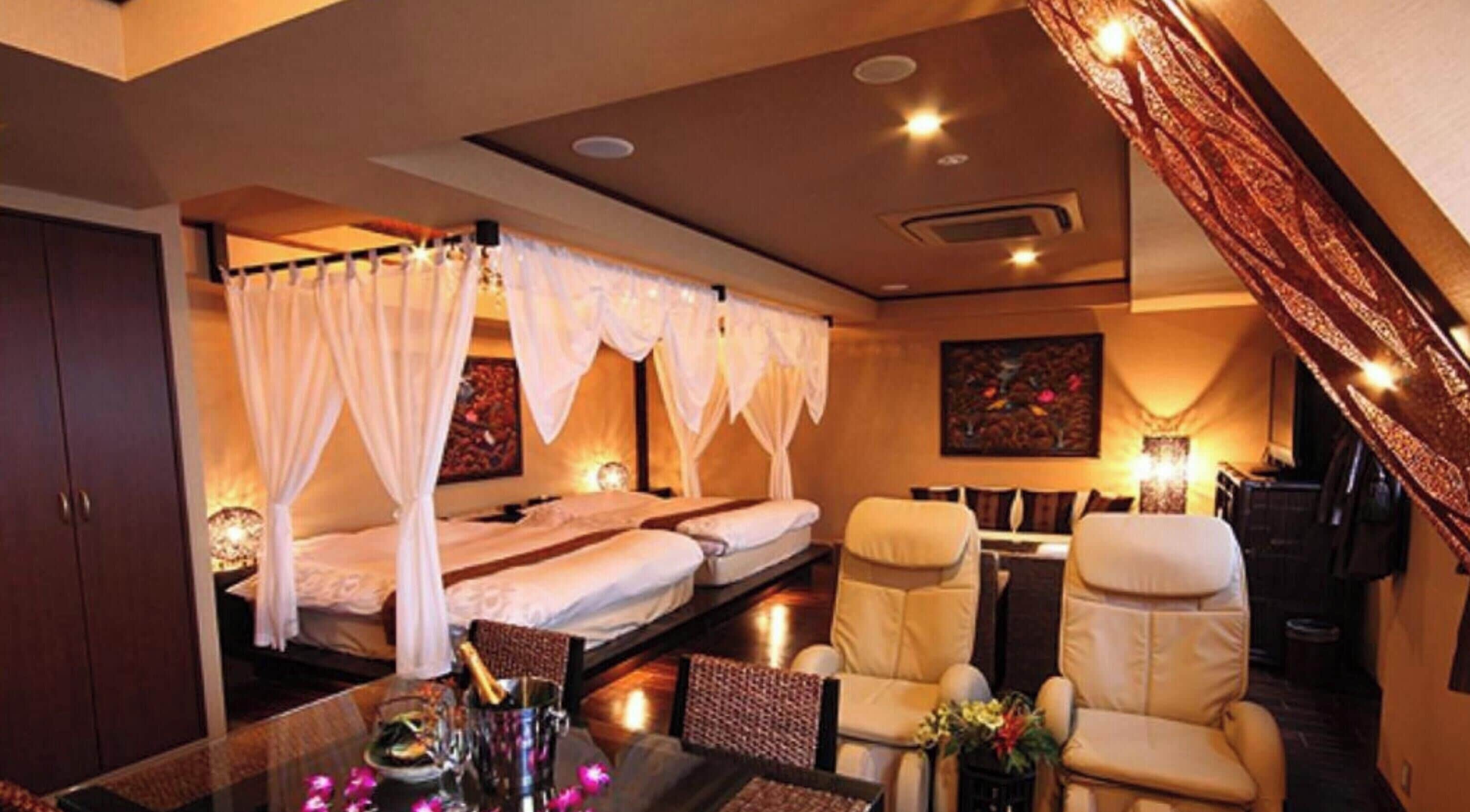 A smoking room with a glass table, two beds with white curtains, a massage chair, and a wall-mounted TV.
