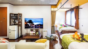 Habitación de hotel con televisión de pantalla plana, dos camas, una kitchenette pequeña y una ventana con cortinas.