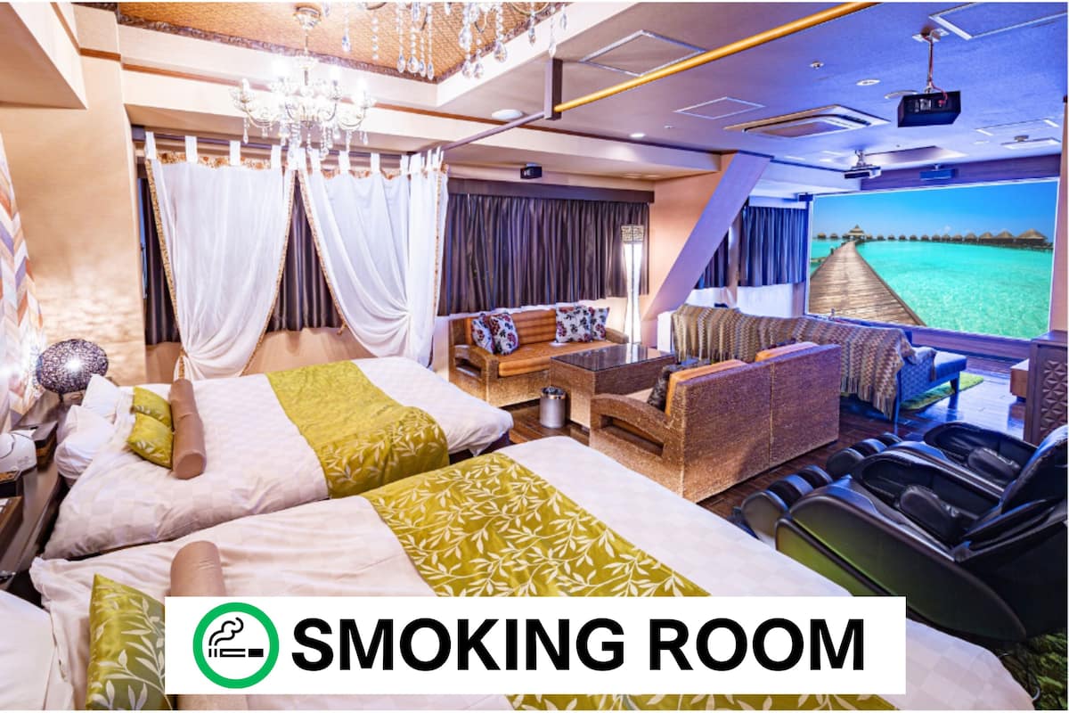 Ein luxuriöses Zimmer mit Bett, Sofa, Massagesesseln und einem großen Bildschirm, der einen Strand zeigt.