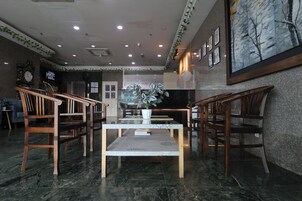 A lobby with a marble floor, wooden chairs, a central table, a clock, and a large painting on the wall.
