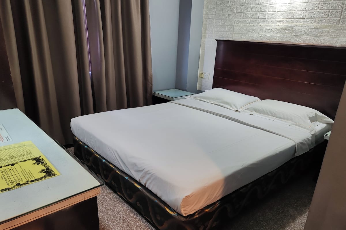 A hotel room with a bed, a small table with a form, a nightstand, and a curtain.