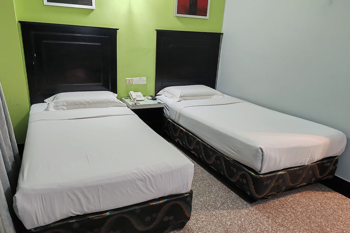 A room with two single beds, each with a black headboard and white bedding. There is a bedside table with a telephone and a power outlet.