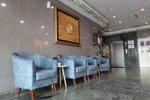 A lobby with a marble floor, blue armchairs, a framed artwork, and a clock on the wall.
