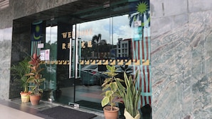 Entrada de hotel con puerta de cristal, letrero de bienvenida y plantas en macetas.