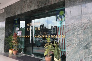 A hotel entrance with a glass door, a welcome sign, and potted plants.