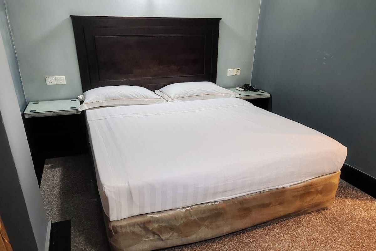 A neatly made bed with white linens, a dark headboard, and a small bedside table with a phone and a lamp.