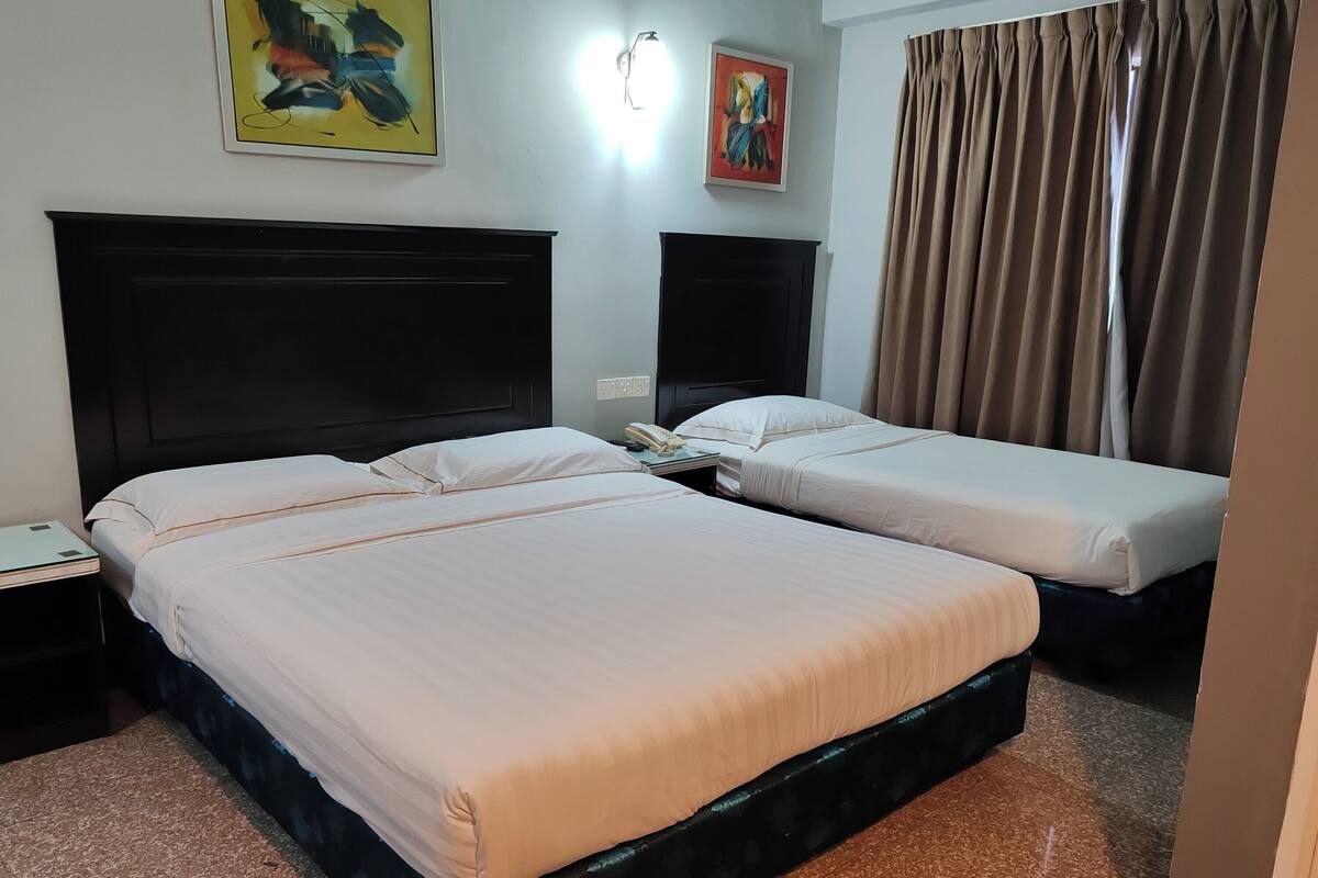 A hotel room with two beds, a nightstand, a wall-mounted lamp, and a painting.