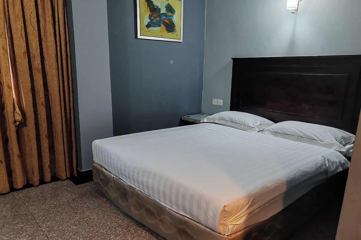 A neatly made bed with a headboard, a wooden curtain, and a wall-mounted abstract painting.