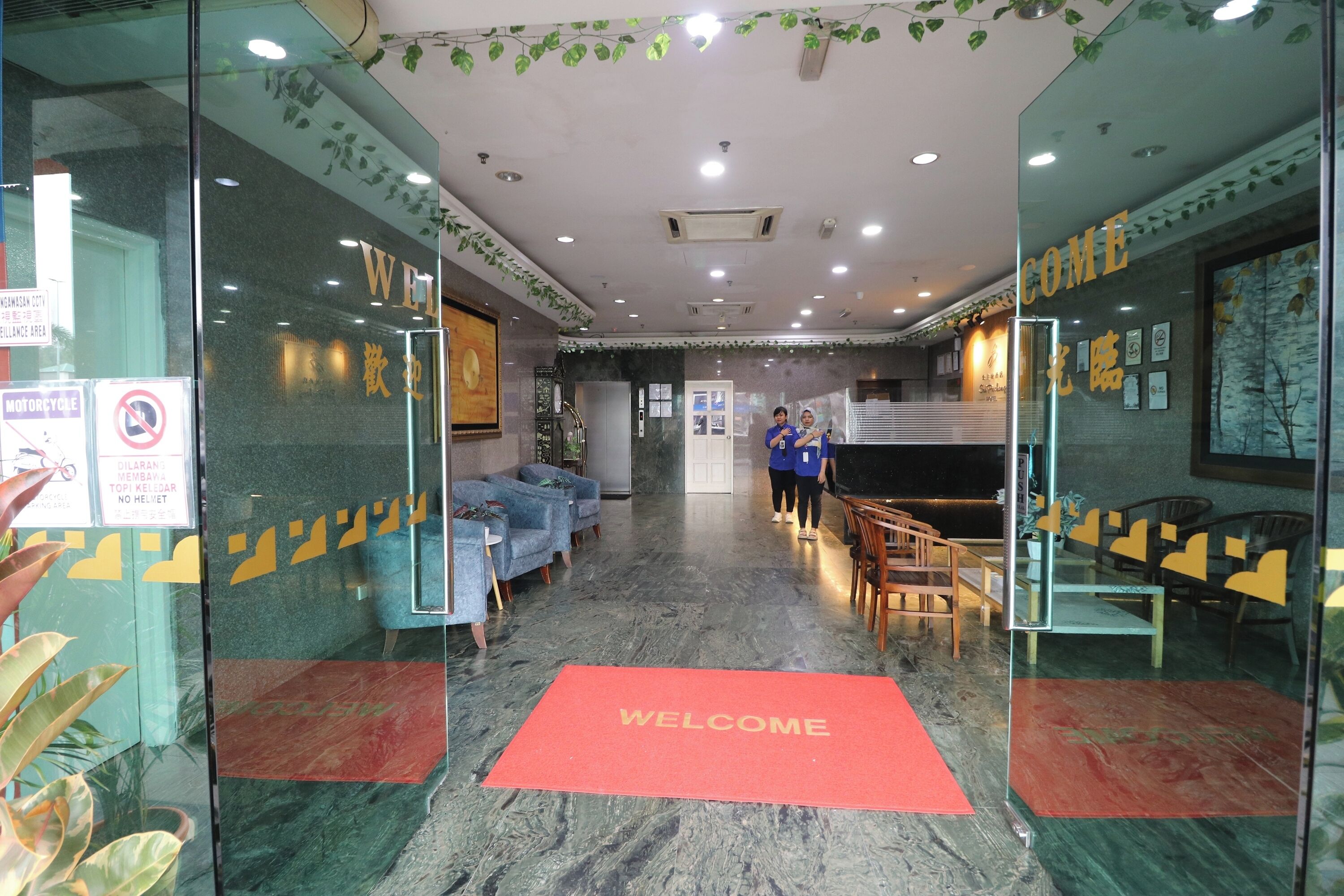 A hotel lobby with a 'WELCOME' mat, seating area, and a reception desk.