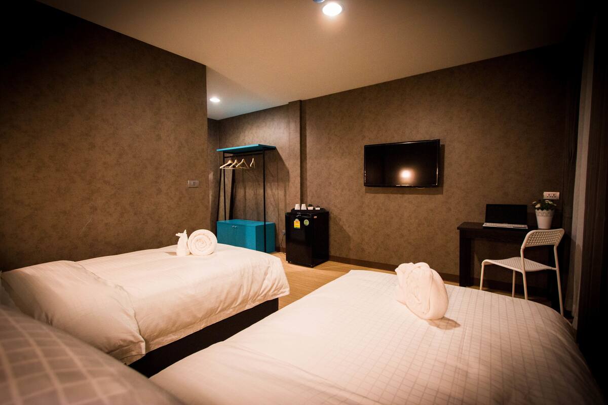 A hotel room with two beds, a TV, a desk with a laptop, a chair, and a coat rack.