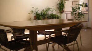 A dining area with a long wooden table surrounded by four wicker chairs, potted plants, and a hanging plant on the wall. - Friendship Motel (George Town)