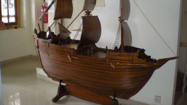 A wooden ship model displayed indoors, with a window and a door in the background. - Friendship Motel (George Town)