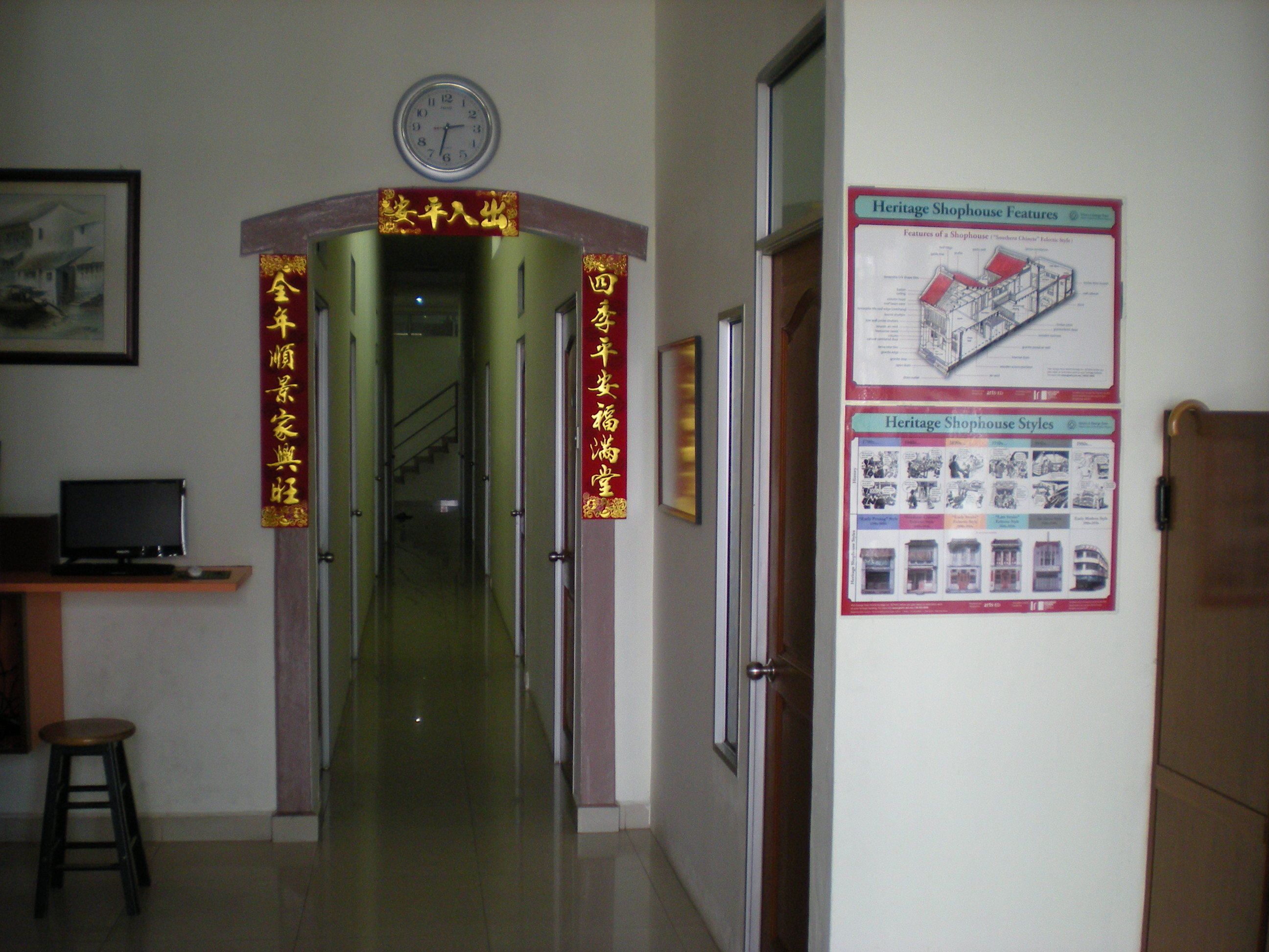 A hallway with a clock on the wall, a poster on the right, and a staircase leading to another room.